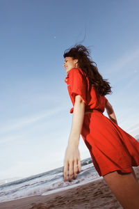 Side view of young woman standing at beach against sky