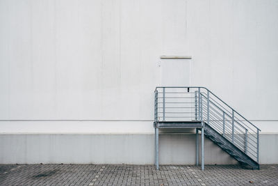 Closed door of an emergency fire exit in a white building wall with gray staircase.