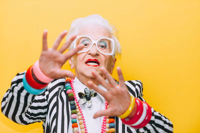 Portrait of senior woman gesturing against yellow background