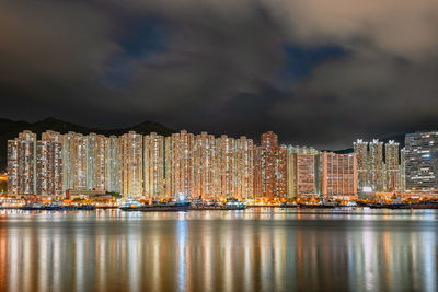 Illuminated buildings by sea against sky at night