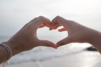 Midsection of woman holding heart shape against sky