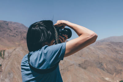 Rear view of man photographing mountains against clear sky
