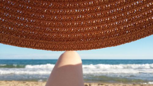 Low section of woman wearing straw hat on beach