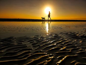 Silhouette man on sea shore against sunset sky