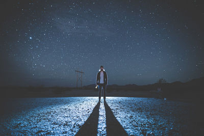 Man standing with long shadow on field against sky at night