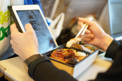 Cropped hand of man using digital tablet while eating lunch