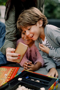 Cropped hand of woman showing mobile phone to children sitting at table