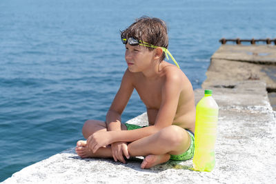 Boy sitting on rock during sunny day