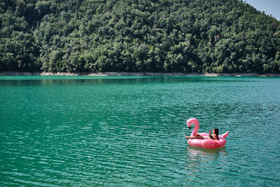 Relaxed female with bottle of refreshing drink lying on inflatable ring in shape of flamingo and floating on lake during summer vacation