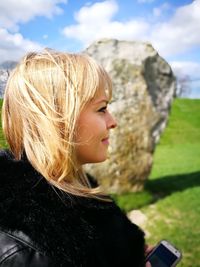 Side view of woman with blond hair wearing black fur jacket at field