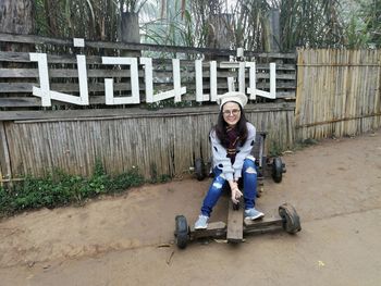 Portrait of smiling woman sitting on abandoned vehicle against fence