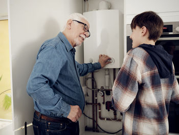 Smiling grandson and grandfather checking boiler for energy saving at home