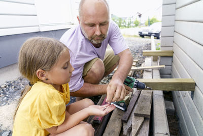 Father and daughter building wooden wall crouching outside house