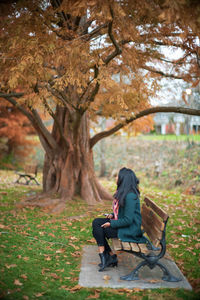 Rear view of woman sitting on bench in park