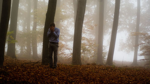 Full length of depressed man standing on field at forest during foggy weather