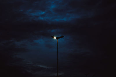 Low angle view of bird perching on illuminated light against sky