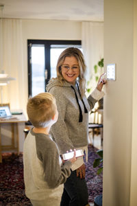 Smiling mother talking to son while using digital tablet mounted on wall at smart home