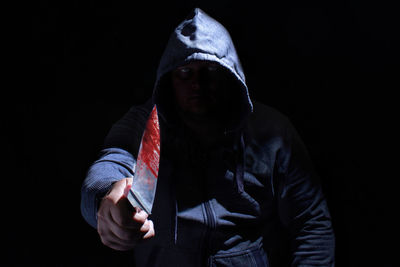 Portrait of criminal holding knife against black background