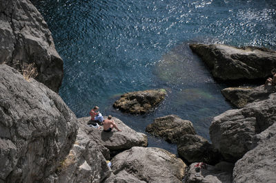 High angle view of couple sitting by sea on rocks