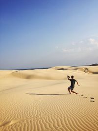 Man on sand dune in desert against clear sky