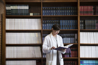 Female scientist reading book by shelves at laboratory