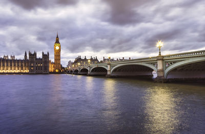 Arch bridge over river by buildings against sky in city