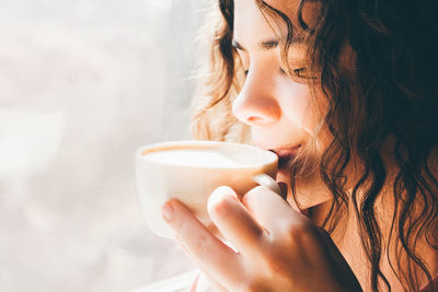 Beautiful woman drinking coffee near the window. close up portrait.