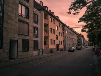 Cars on road by buildings against sky at sunset