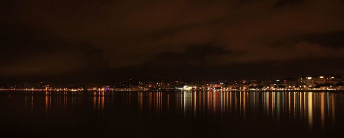 Illuminated cityscape by sea against sky at night