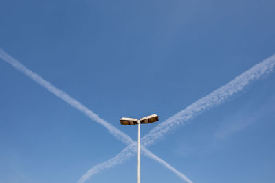 Low angle view of street light with vapor trails against sky