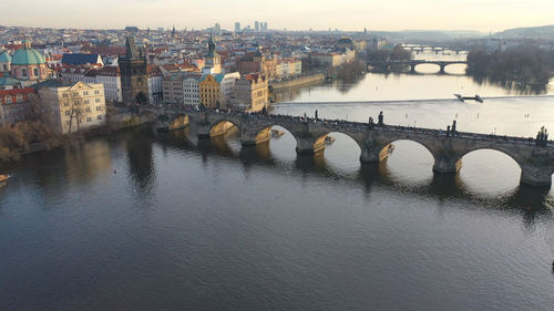 Bridge over river by buildings in city against sky