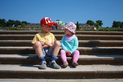 Full length of cute siblings sitting on steps during sunny day