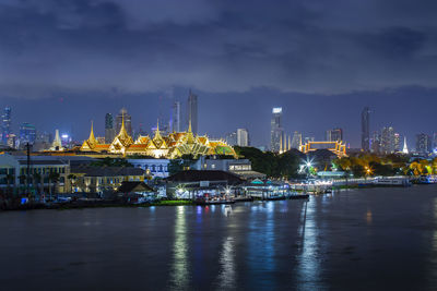 Illuminated city by river against sky at night