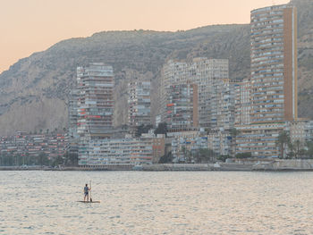 Back view of unrecognizable sporty man swimming on surfboard paddle looking at amazing cityscape in alicante spain