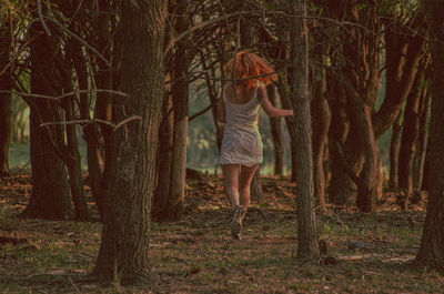 Rear view of woman running by trees in forest