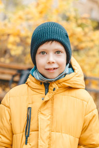 Ortrait of a smiling boy in a hat and a yellow jacket, on the street. walk in the street in autumn
