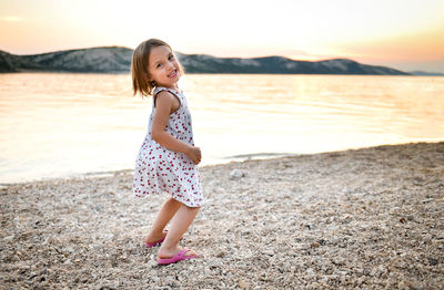 Side view of girl standing on shore at beach during sunset