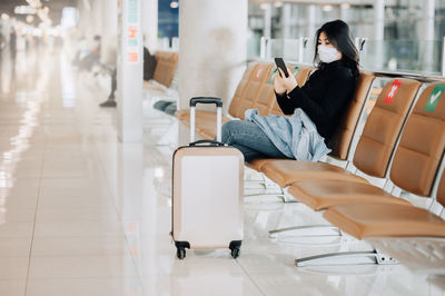 Woman wearing mask sitting on bench at airport