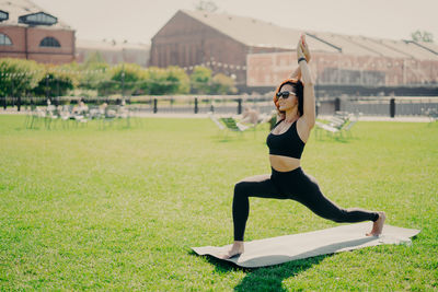 Woman wearing sunglasses exercising on mat in park