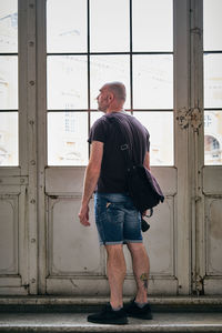 Rear view of man looking away while standing against wall