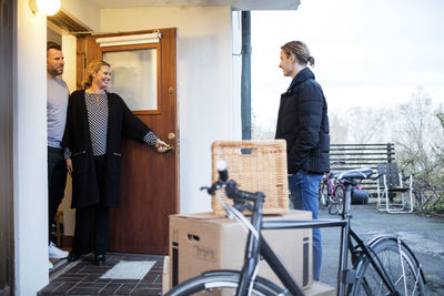 Happy parents looking at son standing by cardboard boxes and bicycle outside new house