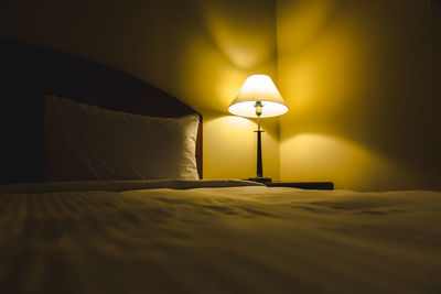 Illuminated lamp on bed against wall at home