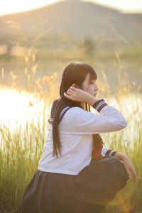 Side view of young woman sitting on field