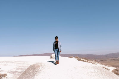 Rear view of woman walking on beach against clear sky