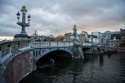 Bridge over river in city against cloudy sky