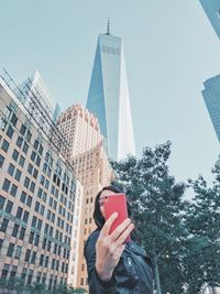 Low angle view of mid adult woman using mobile phone while standing against sky in city