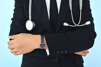 Midsection of doctor with arms crossed while standing against blue background