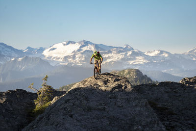 Full length of man cycling on rock against mountain range