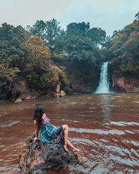 Woman sitting on rock against waterfall