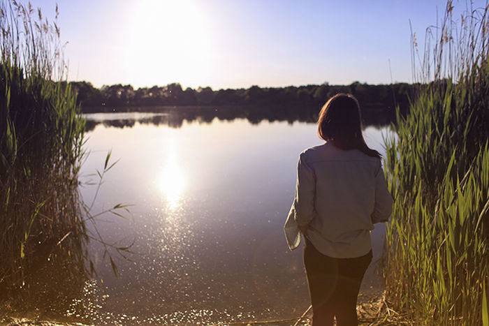 REAR VIEW OF MAN LOOKING AT LAKE ON SUNNY DAY